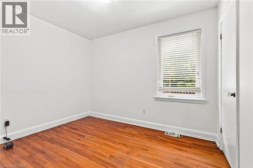 Room featuring wood-finish flooring, white walls, and a single-pane window with adjustable blinds - 241 East 44Th Street, Hamilton, ON 