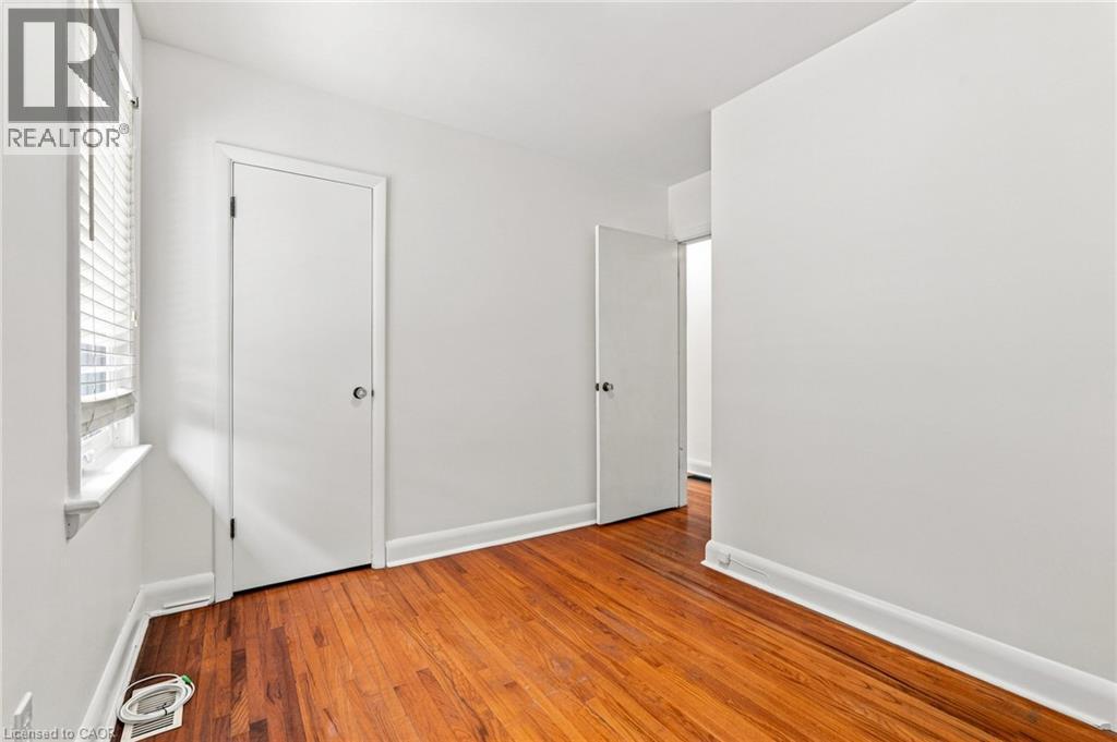 Interior space featuring wood-finish flooring, white walls, and a window with horizontal blinds - 241 East 44Th Street, Hamilton, ON