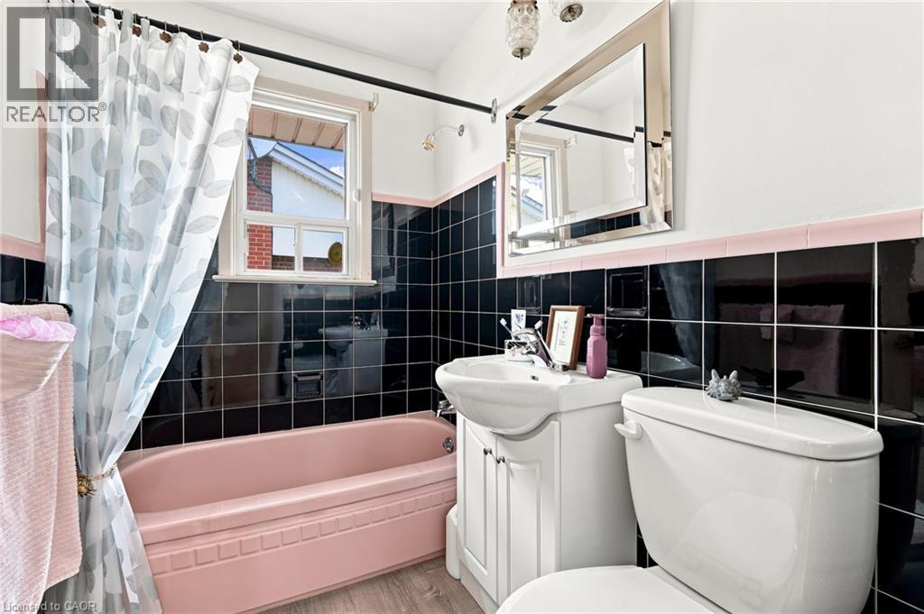 Bathroom featuring black wall tiling with pink tile trim, a pink soaking tub, a white vanity with an integrated sink, and a framed vanity mirror - 241 East 44Th Street, Hamilton, ON