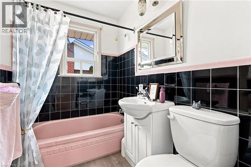 Bathroom featuring black wall tiling with pink tile trim, a pink soaking tub, a white vanity with an integrated sink, and a framed vanity mirror - 241 East 44Th Street, Hamilton, ON 