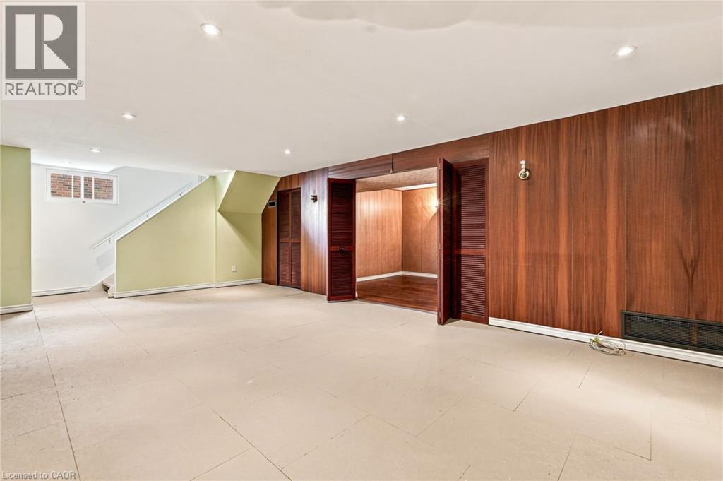 Spacious room featuring wood-panelled walls, recessed ceiling lighting, louvered closet doors, and light-toned tile flooring - 241 East 44Th Street, Hamilton, ON