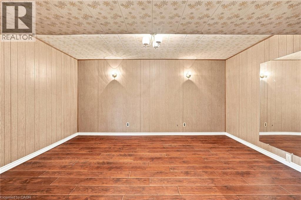 Interior room featuring wood-finish flooring, wood-paneled walls, a ceiling-mounted light fixture, dual wall-mounted sconces, and a large wall-mounted mirror - 241 East 44Th Street, Hamilton, ON