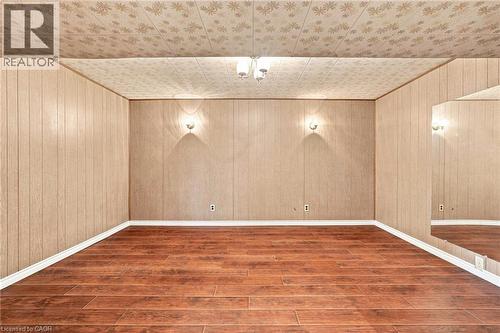 Interior room featuring wood-finish flooring, wood-paneled walls, a ceiling-mounted light fixture, dual wall-mounted sconces, and a large wall-mounted mirror - 241 East 44Th Street, Hamilton, ON 