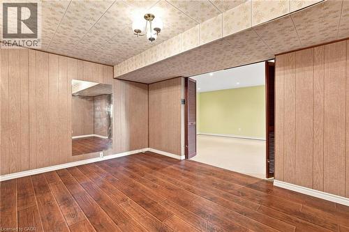 Wood-finish flooring, full-wall mirrored panel, patterned drop ceiling, built-in louvered doors, and three-light flush-mount ceiling fixture - 241 East 44Th Street, Hamilton, ON 