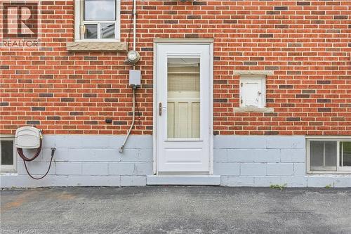 Red brick exterior facade with a painted concrete block foundation, white full-lite entry door, and multiple horizontal windows with stone sills - 241 East 44Th Street, Hamilton, ON 