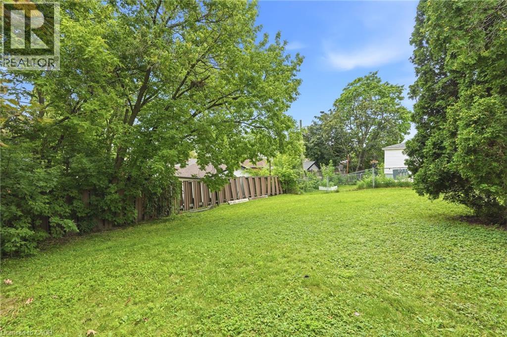 Expansive backyard featuring a grass lawn, mature trees, and wooden perimeter fencing - 241 East 44Th Street, Hamilton, ON