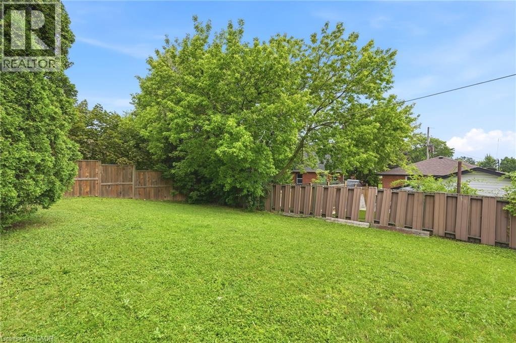 Expansive backyard featuring a level lawn, mature shade trees, and perimeter wood fencing - 241 East 44Th Street, Hamilton, ON