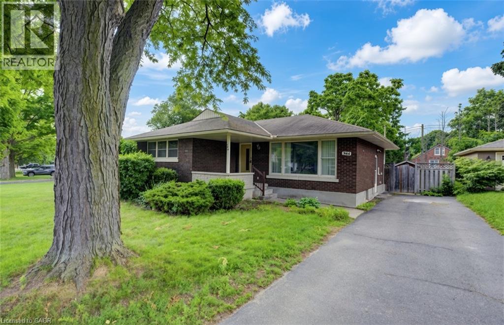Single-story brick exterior featuring a covered front entryway, expansive lawn, mature tree, and asphalt driveway - 244 Royal Street, Waterloo, ON