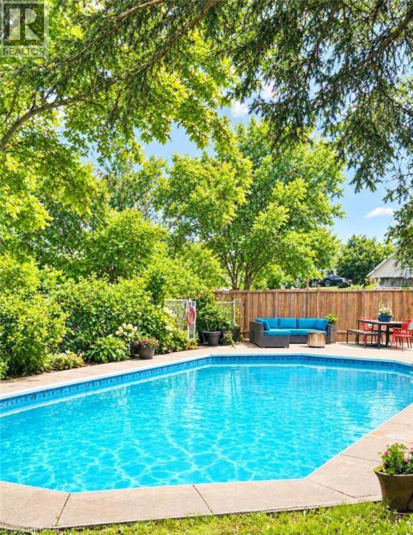 In-ground swimming pool with concrete patio surround, mature trees, and wooden perimeter fencing - 361 Lee Circle, Waterloo, ON