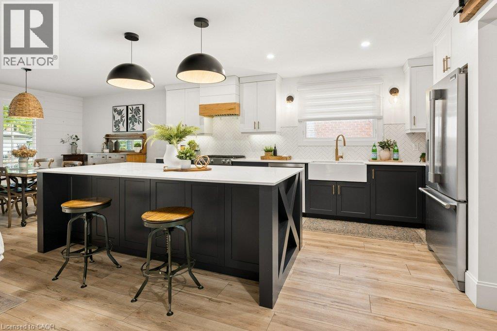 Kitchen featuring a central island with a solid-surface countertop, apron-front farmhouse sink, herringbone-pattern tile backsplash, wood-finish flooring, and two-tone cabinetry - 361 Lee Circle, Waterloo, ON