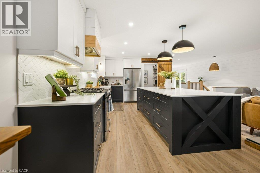Kitchen featuring white and black shaker-style cabinetry, white stone-finish countertops, a large island with X-frame detailing, herringbone-patterned tile backsplash, and wood-finish flooring - 361 Lee Circle, Waterloo, ON