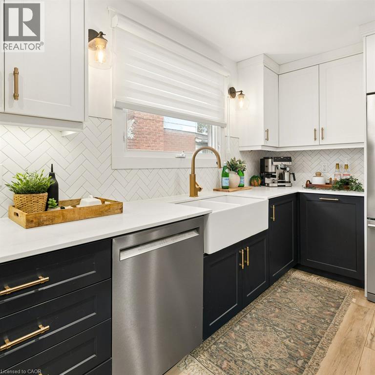 Kitchen featuring two-tone cabinetry with brass-finish hardware, quartz countertops, herringbone tile backsplash, and a white farmhouse sink with a brass-finish faucet - 361 Lee Circle, Waterloo, ON