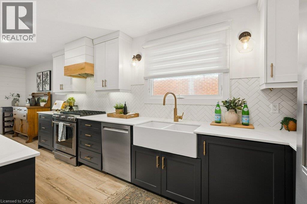 Kitchen featuring two-tone cabinetry, farmhouse sink with brass-finish faucet, herringbone-patterned tile backsplash, wood-finish flooring, and a custom range hood - 361 Lee Circle, Waterloo, ON