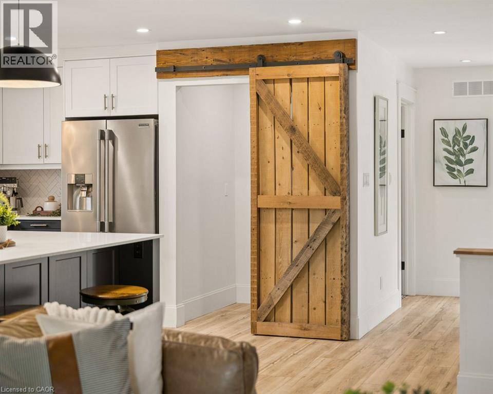 Custom sliding barn door with exposed hardware, stainless steel refrigerator, white cabinetry, and wood-finish flooring - 361 Lee Circle, Waterloo, ON
