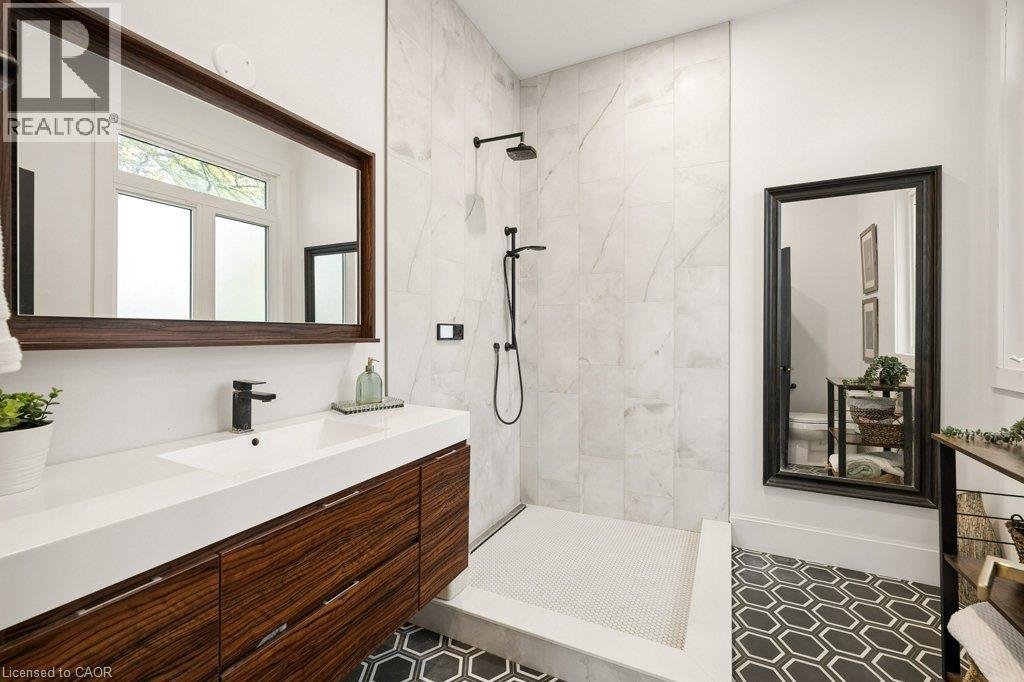 Bathroom featuring a dark wood-finish vanity with an integrated basin, walk-in shower with large-format wall tile, matte black rainfall showerhead, and geometric patterned floor tile - 361 Lee Circle, Waterloo, ON