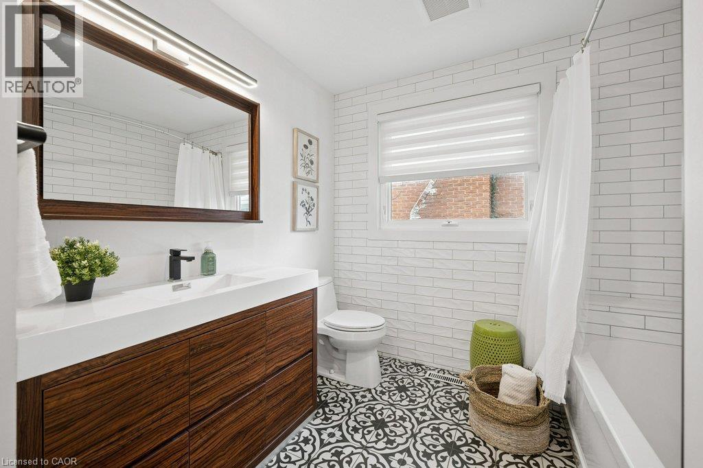 Bathroom featuring a wood-finish vanity with a rectangular sink, matte black faucet, patterned tile flooring, and white subway-style wall tile - 361 Lee Circle, Waterloo, ON