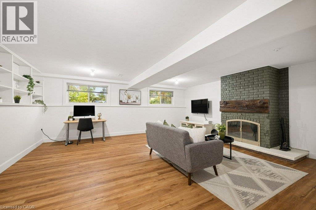 Painted brick fireplace with a rustic timber mantel and stone hearth, wood-finish flooring, built-in shelving, and recessed ceiling lighting - 361 Lee Circle, Waterloo, ON