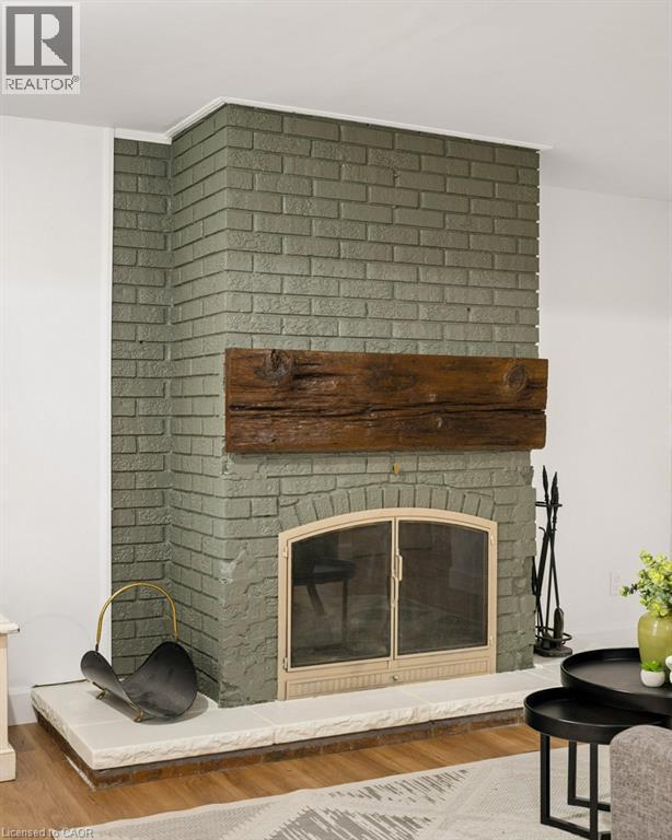 Painted brick fireplace featuring an arched firebox, metallic glass-paneled screen, and a substantial reclaimed timber mantel set upon a raised stone hearth - 361 Lee Circle, Waterloo, ON