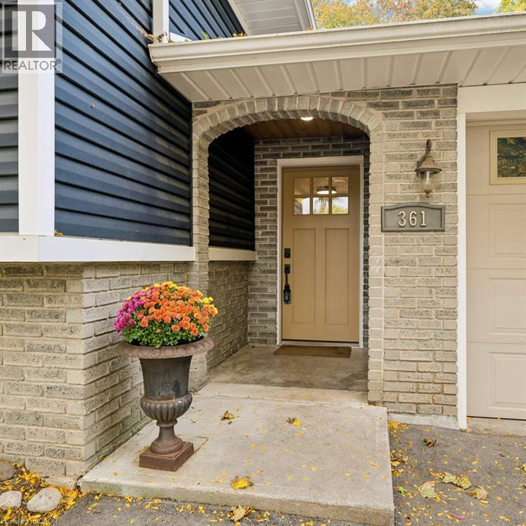 Exterior entry featuring a recessed archway with brick masonry, navy horizontal siding, a paneled door with multi-lite glass upper, and a wall-mounted exterior light fixture - 361 Lee Circle, Waterloo, ON