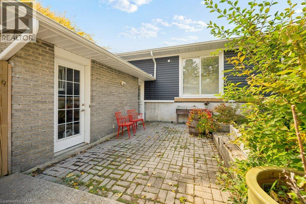 Exterior patio featuring brick paver hardscaping, light-toned masonry siding, horizontal vinyl cladding, and a white-framed glass paneled door - 361 Lee Circle, Waterloo, ON