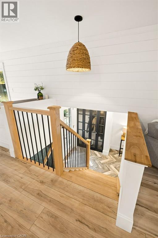 Staircase featuring wood-finish flooring, white shiplap walls, a natural fiber woven pendant light, and a railing with wooden handrails and black metal balusters - 361 Lee Circle, Waterloo, ON
