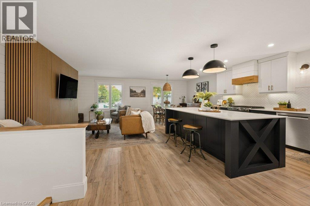 Open-concept kitchen featuring a center island with contrasting cabinetry, wood-finish flooring, a vertical slat wood accent wall, and farmhouse-style recessed lighting - 361 Lee Circle, Waterloo, ON