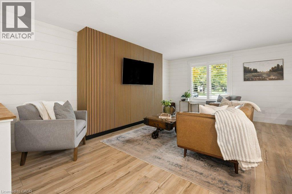 Bright, open living space featuring warm wood-finish flooring, a custom wood-slat accent wall with integrated flat-screen television, and large windows with natural light - 361 Lee Circle, Waterloo, ON