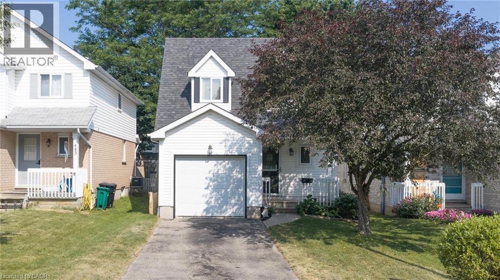 Two-story exterior featuring white vinyl siding, a front-facing single-car garage, a steep-pitched roofline with a dormer window, and an asphalt driveway - 449 Exmoor Street, Waterloo, ON