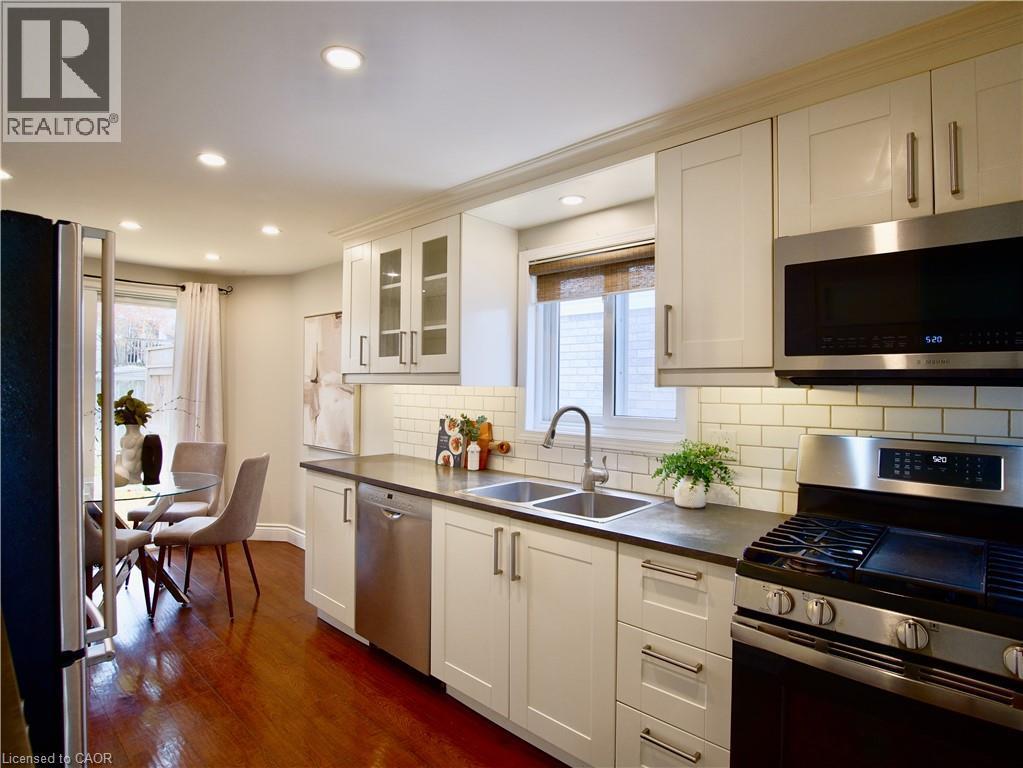Kitchen featuring white cabinetry, subway tile backsplash, dark countertops, stainless steel appliances, and recessed lighting - 449 Exmoor Street, Waterloo, ON