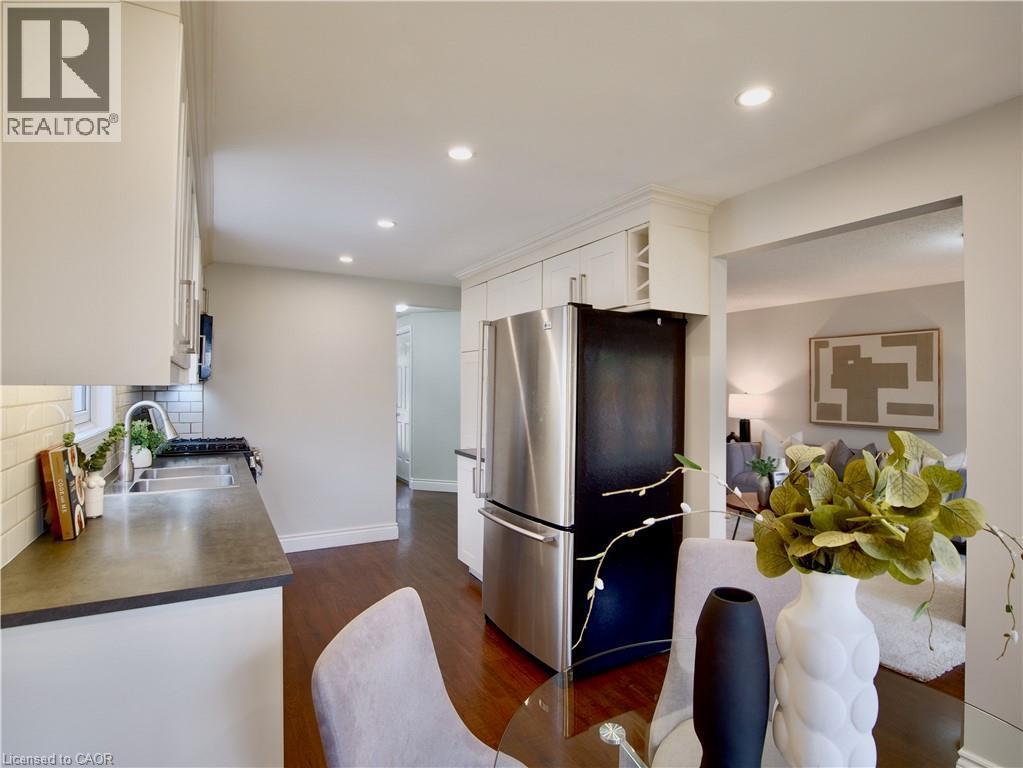 Kitchen featuring white cabinetry, wood-finish flooring, recessed lighting, stainless steel refrigerator, and dual-basin sink with tile backsplash - 449 Exmoor Street, Waterloo, ON