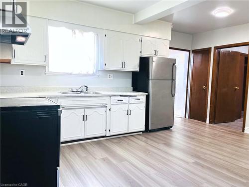 Kitchen featuring white cabinetry, stainless steel refrigerator, wood-finish flooring, and a double-basin sink - 1279 Hamilton Street, Cambridge, ON 