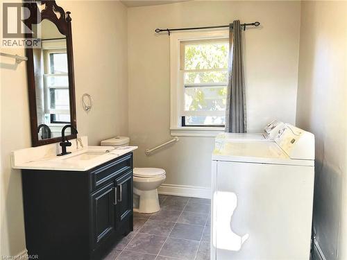 Dark-toned vanity with a white countertop and matte black faucet, wall-mounted mirror, white ceramic toilet, and tile flooring - 1279 Hamilton Street, Cambridge, ON 