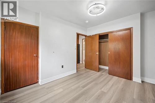Interior room featuring wood-finish flooring, solid wood-veneer doors, integrated closet shelving, and a modern circular flush-mount ceiling light fixture - 1279 Hamilton Street, Cambridge, ON 