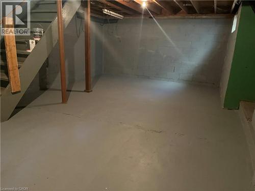 Unfinished lower level featuring painted concrete block walls, painted concrete flooring, exposed ceiling joists, and a wooden staircase - 1279 Hamilton Street, Cambridge, ON 