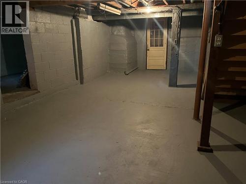 Unfinished storage area featuring painted concrete block walls, painted concrete flooring, an exposed ceiling structure, and a multi-pane door - 1279 Hamilton Street, Cambridge, ON 