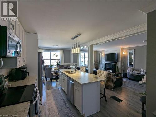 Kitchen island with dual-basin undermount sink and stone countertop, wood-finish flooring, white cabinetry, integrated stainless steel appliances, and ceiling-mounted pendant lighting - 326 Ottawa Street, Hamilton, ON 