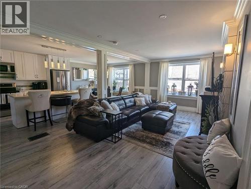 Open-concept kitchen and living area featuring white cabinetry, a center island with pendant lighting, wood-finish flooring, and crown molding - 326 Ottawa Street, Hamilton, ON 
