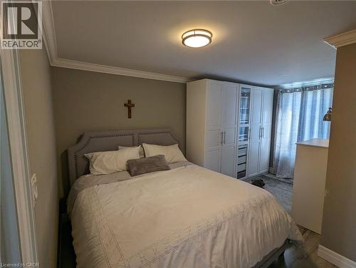 Bedroom featuring crown molding, built-in floor-to-ceiling cabinetry with glass-panel detailing, and wood-finish flooring - 326 Ottawa Street, Hamilton, ON 