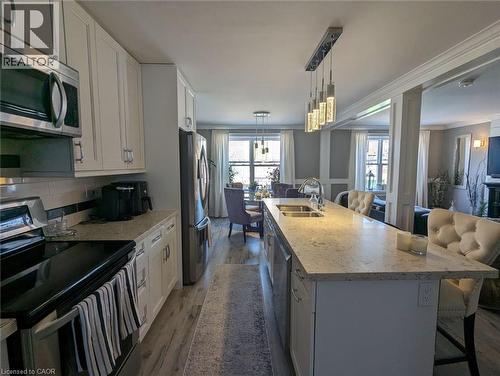 Kitchen featuring shaker-style cabinetry, stainless steel appliances, quartz countertops, a central island with integrated sink, and wood-finish flooring - 326 Ottawa Street, Hamilton, ON 