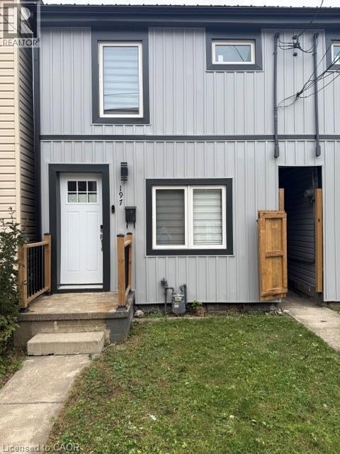 Exterior facade featuring vertical metal siding with dark-trimmed windows, a multi-pane front door, and a concrete entry stoop with wooden railings - 197 Ferguson Avenue S, Hamilton, ON