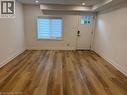 Room featuring wood-finish flooring, recessed lighting, white walls, a single-hung window with installed blinds, and an exterior door with a glass pane - 197 Ferguson Avenue S, Hamilton, ON 