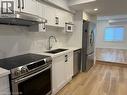 Kitchen featuring shaker-style cabinetry, quartz countertops, full-height stone-patterned backsplash, stainless steel appliances, and wood-finish flooring - 197 Ferguson Avenue S, Hamilton, ON 