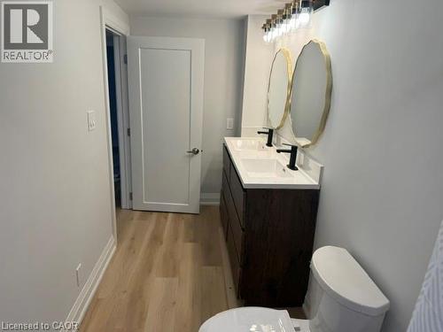 Double vanity with wood-finish cabinetry, rectangular integrated sinks, stone-surface countertop, and matte black hardware - 197 Ferguson Avenue S, Hamilton, ON 