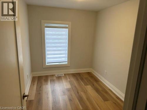 Interior room featuring wood-finish flooring, light neutral walls, and a window with installed roller shades - 197 Ferguson Avenue S, Hamilton, ON 