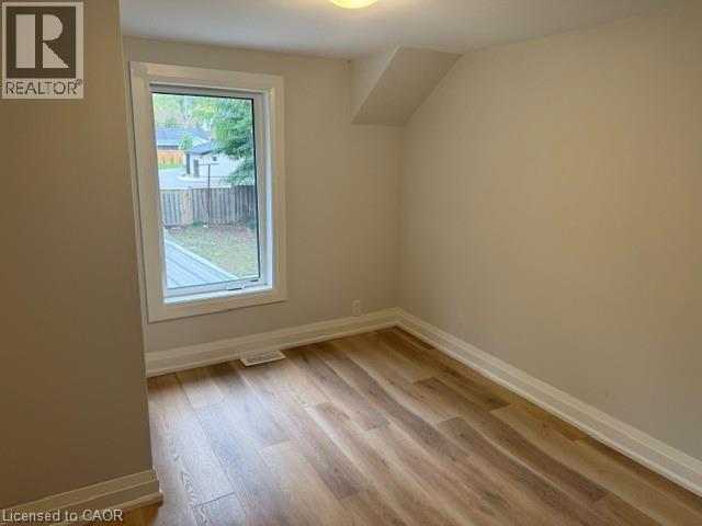 Neutral interior featuring wood-finish flooring, a single pane window with white trim, and a sloped ceiling detail - 197 Ferguson Avenue S, Hamilton, ON