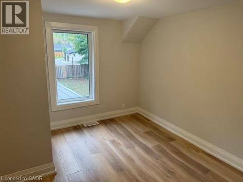 Neutral interior featuring wood-finish flooring, a single pane window with white trim, and a sloped ceiling detail - 197 Ferguson Avenue S, Hamilton, ON 