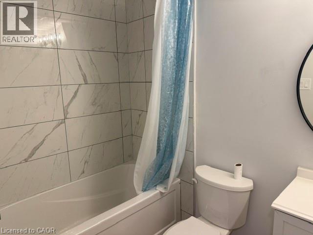 Bathroom featuring full-height large-format wall tile with a veined pattern, built-in bathtub, and a circular wall-mounted mirror - 197 Ferguson Avenue S, Hamilton, ON