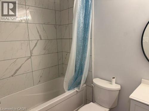 Bathroom featuring full-height large-format wall tile with a veined pattern, built-in bathtub, and a circular wall-mounted mirror - 197 Ferguson Avenue S, Hamilton, ON 