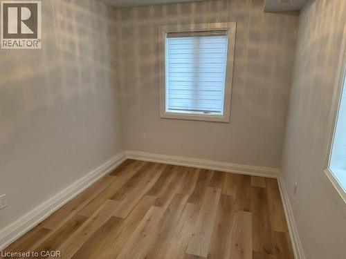Neutral-toned room featuring wood-finish flooring and a window with installed roller shades - 197 Ferguson Avenue S, Hamilton, ON 