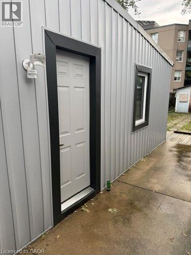 Exterior featuring vertical metal panel siding, a six-panel door with high-contrast trim, a single window, and a dual-head wall-mounted light fixture - 197 Ferguson Avenue S, Hamilton, ON 